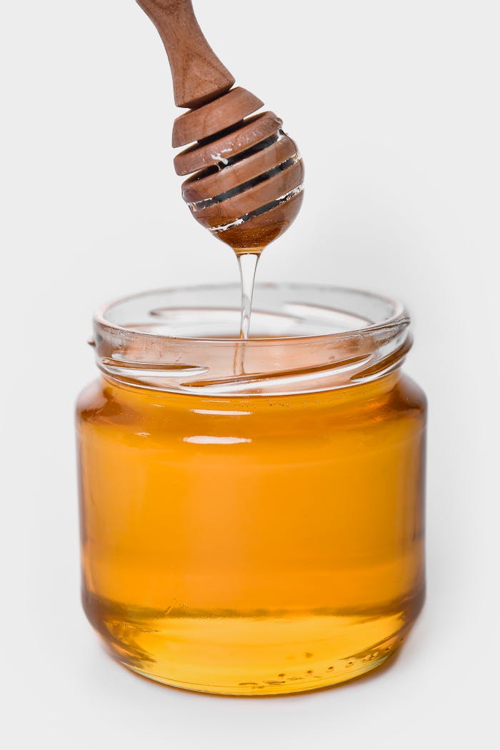 Rich golden honey dripping from a wooden dipper into a glass jar, highlighting its sweet and sticky texture.