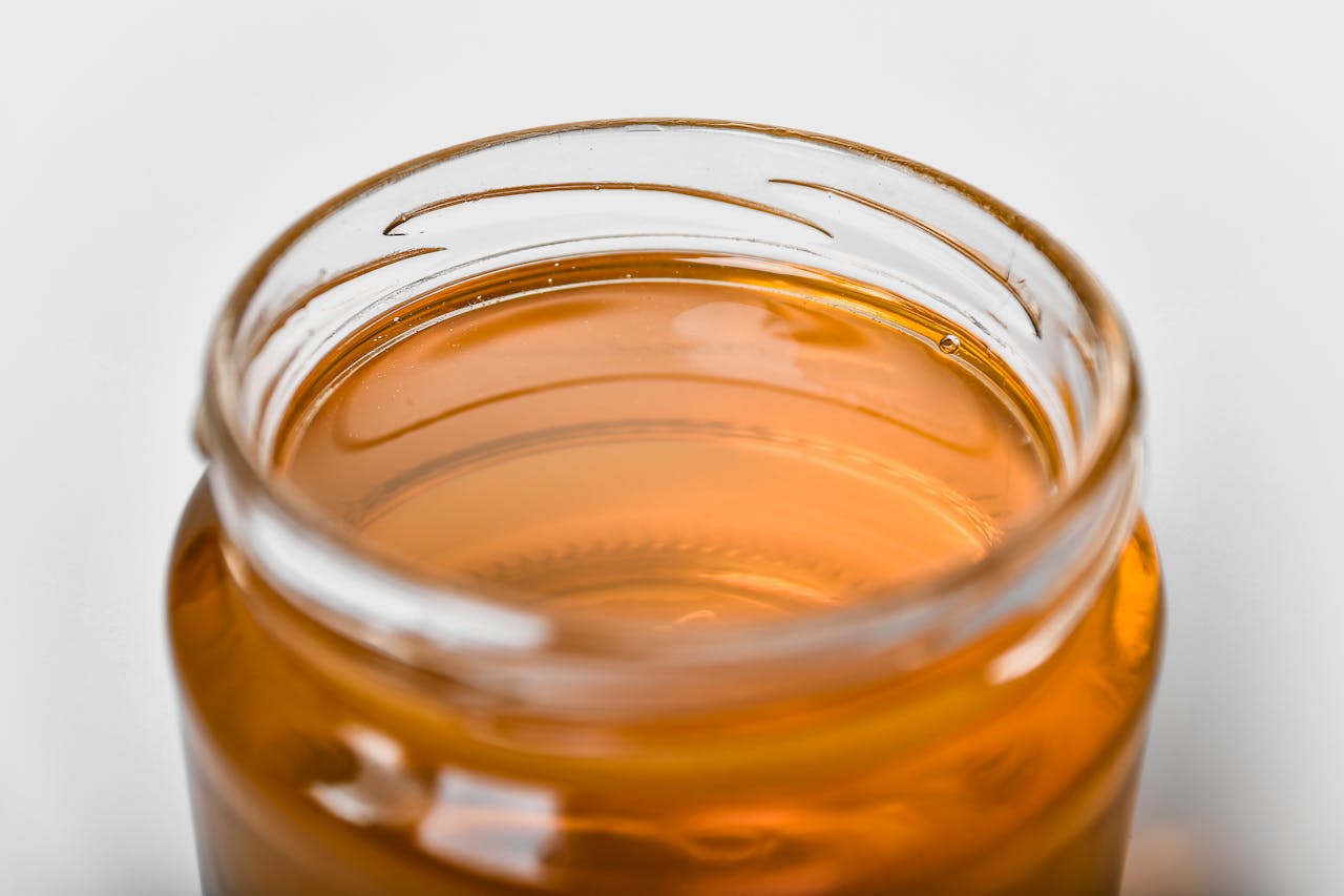 Close-up of a jar filled with golden honey, emphasizing its smooth texture and shimmering hue.