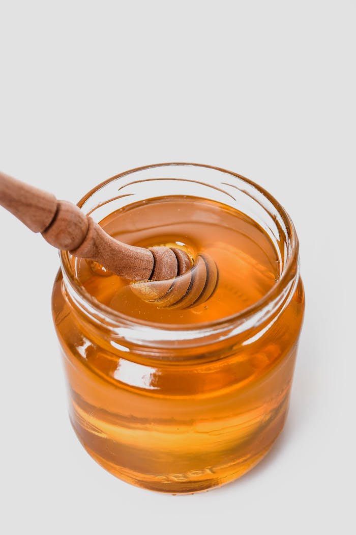 Close-up of golden honey in a glass jar with a wooden honey dipper.