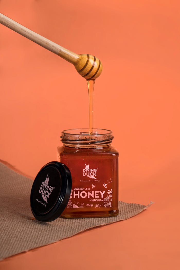 Close-up of a honey dipper and jar on an orange background, perfect for culinary uses.