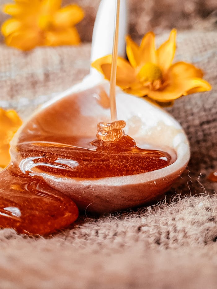 Golden honey dripping from a spoon with yellow flowers for a natural, sweet aesthetic.
