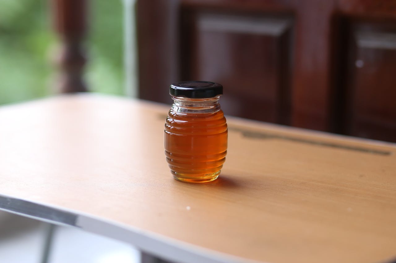 A small glass jar filled with golden honey on a wooden table, offering a sweet treat concept.
